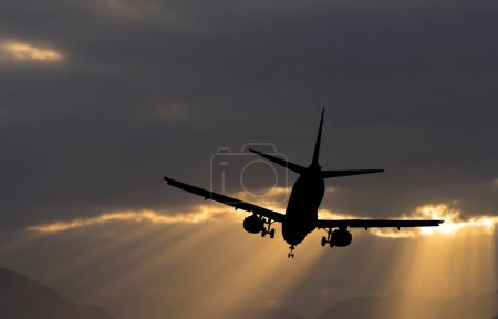 Silhouette of landing airplane in the early morning with beams of sunlight