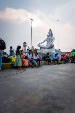 Téléchargez les photos : 4 juillet 2022 Haridwar Inde. Statue du Seigneur Shiva à la gare de Haridwar avec des gens assis tout autour dans l'attente. - en image libre de droit