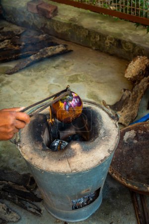 Photo for Whole roasted eggplant or brinjal in a traditional clay stove, Angeethi in Northern India. Preparation of a North Indian cuisine, Baigan ka Bharta. India - Royalty Free Image