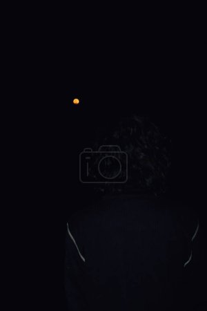 Foto de Noche oscura en la India: silueta de un hombre hipnotizado por el brillo de una luna llena de sangre durante un eclipse lunar total - Imagen libre de derechos