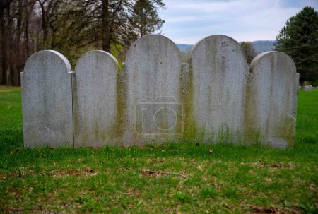 Téléchargez les photos : Cinq pierres tombales grises reliées en arc de différentes tailles côte à côte dans un cimetière herbeux Tourné à la lumière naturelle avec espace de copie et personne. - en image libre de droit