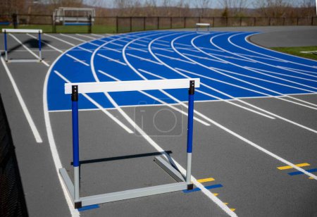 Photo for Beautiful athletic track with fresh paint and track surface texture. Hurdles set up on the lane markers with curving track behind - Royalty Free Image