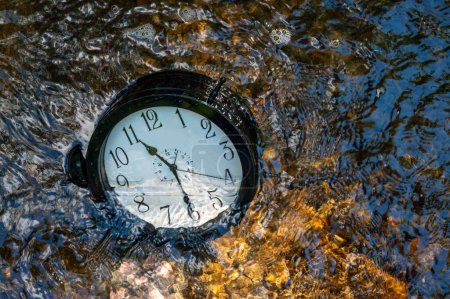 Photo for Concept image losing track of time, relativity science image, flowing time, large clock in a flowing stream with half of the clock face submerged with ripples and colors distorting the numbers. Ouitdoors with no people and copy space. - Royalty Free Image