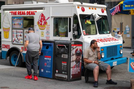 Téléchargez les photos : New York, NY, USA, 19-07-2023 Un homme est assis sur une caisse de lait fumant une cigarette à côté d'un camion de crème glacée Frostee garé le long d'une rue de Manhattan avec des piétons et un drapeau américain. Le Real Deal - en image libre de droit