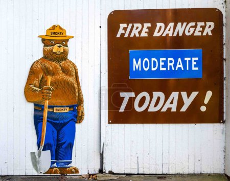 Foto de Shillington, PA, USA 10-11-2023 Señalización de peligro de incendio y colorido cartel de Smokey the Bear de tamaño natural en el fondo de la puerta de madera blanca al aire libre en el parque estatal Nolde Forest Pennsylvania - Imagen libre de derechos