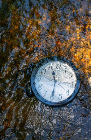 Photo for Concept image losing track of time, relativity science image, flowing time, large clock in a flowing stream with half of the clock face submerged with ripples and colors distorting the numbers. Ouitdoors with no people and copy space. - Royalty Free Image
