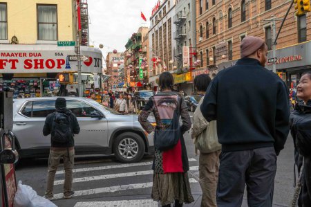 Foto de Nueva York, NY, Estados Unidos 11-09-2023 Mujer con una elegante chaqueta artística decorada con un gran ojo de trippy espera para cruzar una concurrida intersección en una calle Chinatown. Uso editorial solamente. - Imagen libre de derechos