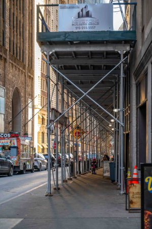 Foto de Nueva York, NY, Estados Unidos 02-20-2023 Los peatones caminan a través de andamios gométricos metálicos a la luz del sol de la hora dorada de Manhattan con edificios de la calle de la ciudad y el camión de comida de tacos. Uso editorial solamente. - Imagen libre de derechos