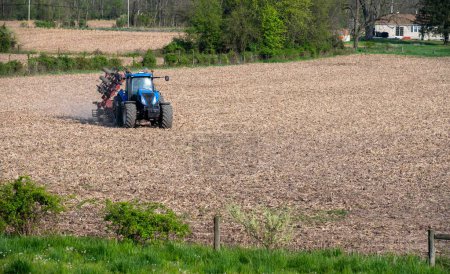 Rural lndscape with agricultural scene soil preparation with disk cultivator tilling farm field for food production. Green woods nature background great colors and texture with copy space