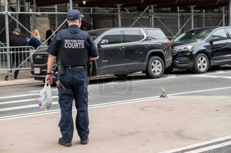 Photo for New York, NY, USA 05-14-2024 A solitary New York State Police officer stands on the street outside courthouse during Trump trial in Manhattan courthouse. Black SUVs in background and defocuased people. Editorial use only. - Royalty Free Image
