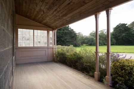 Textura de fondo de una veranda de madera con suelo de madera y techo en el porche delantero unido fuera de una casa de campo de piedra frente a un gran espacio verde abierto. Copiar espacio para su diseño. 