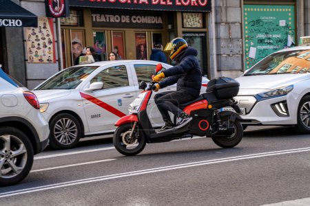 Photo for Electric motorcycle of the company acciona for rent by the minute driven along gran via street in madrid between several cars and cabs. - Royalty Free Image