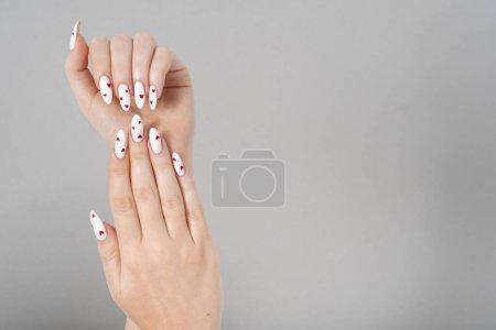 Foto de Manicura femenina dos manos gel mínimo esmalte blanco uñas largas y corazones rojos diseñando fondo aislado gris. Spa de belleza, San Valentín, concepto de amor - Imagen libre de derechos