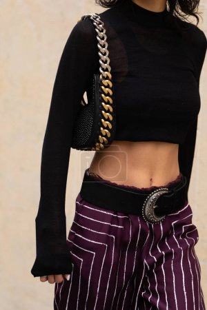 Photo for Paris, France - October, 3, 2022: woman wears black high neck long sleeves cropped top, leather belt, burgundy with white striped pants, gold chain handbag from Stella McCartney, street style details. - Royalty Free Image