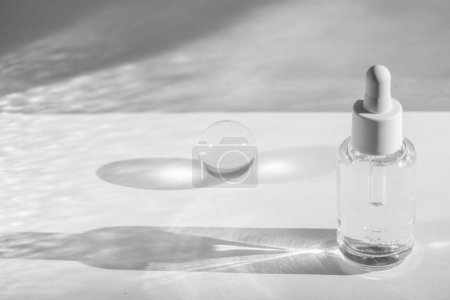 Flacon de sérum clair et boule de cristal coulant des ombres délicates sur fond blanc, soins cosmétiques de beauté