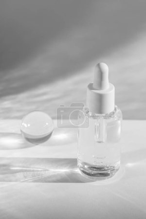 klare Serumflasche und Kristallkugel schaffen elegante Schatten auf weißem Hintergrund, kosmetische Vitrine