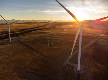 Foto de Molinos de viento aéreos al atardecer con rayos solares produciendo energía sostenible en las praderas de Alberta en Canadá. - Imagen libre de derechos
