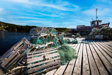 Foto de Summerville Terranova Canadá, 23 de septiembre de 2022: Trampas de langosta de madera apiladas en un muelle con barcos de pesca fuera del agua en un pequeño pueblo pesquero atlántico. - Imagen libre de derechos