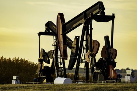 Téléchargez les photos : Pump Jacks travaillant sur des terres agricoles appartenant à des sociétés pétrolières et gazières au coucher du soleil dans le comté de Rocky View Alberta Canada. - en image libre de droit