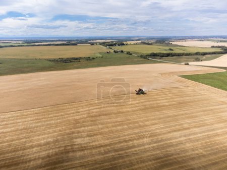 Distant harvester high aerial working on an agriculture field with dust trail on the Canadian prairies overlooking farmlands in Alberta Canada.