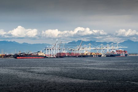 Foto de Delta British Columbia Canada, 23 de julio de 2023: Se cargan pilas de carbón en un carguero y se descargan buques portacontenedores en una terminal de transporte. - Imagen libre de derechos