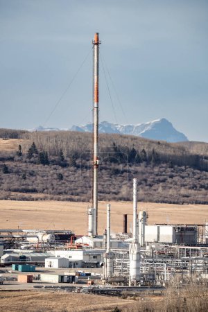 Téléchargez les photos : Usine de gaz rurale de l'Alberta avec cheminée et équipement industriel vue de portrait surplombant la colline et la montagne près de Cochrane Alberta Canada - en image libre de droit