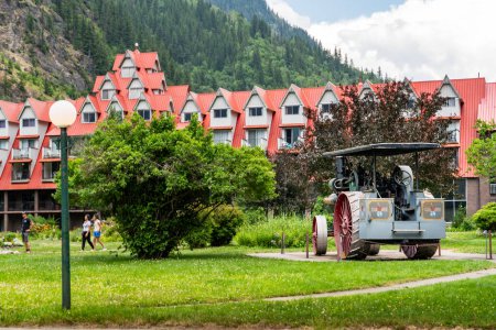 Photo for Three Valley Gap British Columbia Canada, July 12 2023: Antique tractor parked in a garden overlooking tourists on a walking path and lake Chateau Hotel at Background. - Royalty Free Image