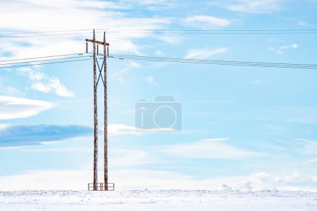 Foto de Poste aislado en un campo de pradera cubierto de nieve con líneas eléctricas aéreas y cables en las praderas canadienses en Rocky View County Alberta. - Imagen libre de derechos
