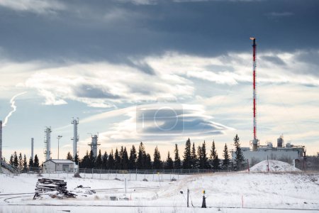 Foto de Planta de petróleo y gas con chimenea bajo un cielo invernal dramático en el oeste de Canadá. - Imagen libre de derechos