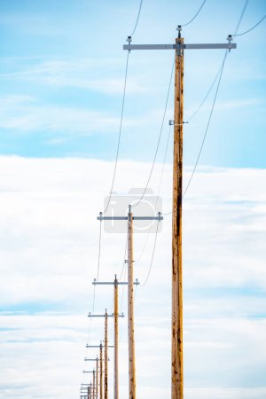 Porträtansicht einer Reihe von Telefonmasten aus Holz mit isolierten Kabeln vor blauem Himmel in Nordamerika.
