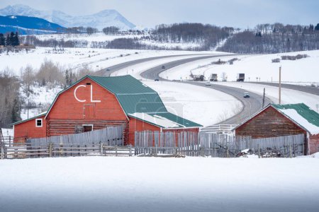 Photo for Rocky View County Alberta Canada, February 2 2024: Red barn and farm houses overlooking the Trans Canada Highway with travellers heading to the Rocky Mountains West of Calgary. - Royalty Free Image
