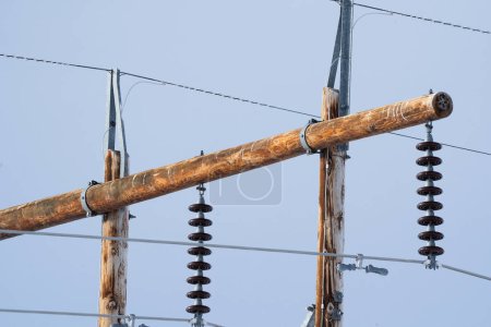 Téléchargez les photos : Vue rapprochée du poteau électrique en bois avec câbles en acier et isolateurs avec fond bleu ciel. - en image libre de droit