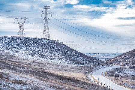 Strommasten auf einem Hügel mit Stromleitungen hängen über einem Tal mit Blick auf eine kurvenreiche Straße in Alberta Kanada.