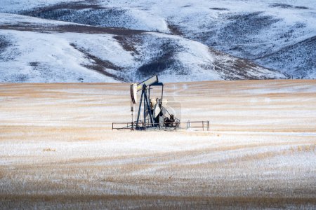 Oil well pump jack sits dormant on a wheat field during winter on the Alberta prairies.