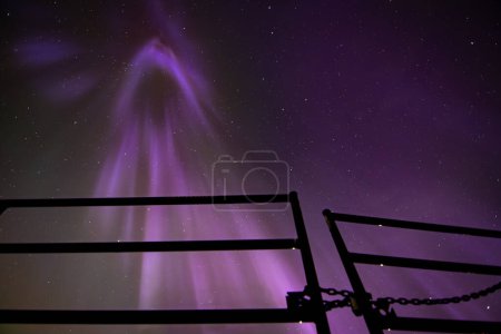 Luces boreales cayendo desde el cielo nocturno con silueta de puerta metálica durante un evento de llamarada solar de nivel cinco.