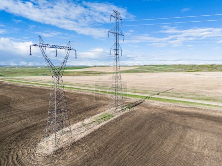 Electrical transmission towers pair aerial shot overlooking agriculture fields and country road in Rocky View County Alberta Canada.