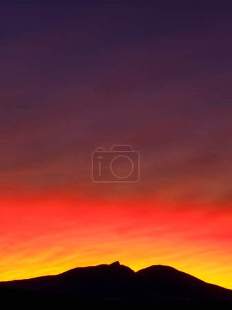 The orange and red sky at dawn casts a dramatic beauty over the silhouetted mountain landscape, creating an atmosphere of tranquil afterglow in this wintery Norwegian environment.