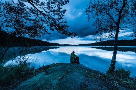 Photo for Lonely man sitting besides lake at blue hour - Royalty Free Image