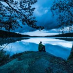 Lonely man sitting besides lake at blue hour