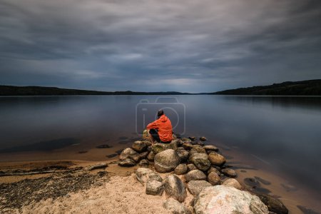 Téléchargez les photos : Homme seul assis au lac immobile - en image libre de droit