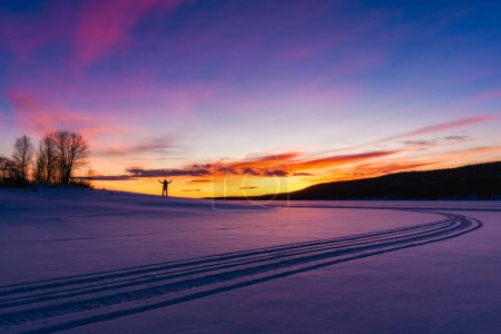 Mann steht bei Sonnenaufgang auf zugefrorenem und schneebedecktem See