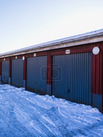 Téléchargez les photos : Rangée de garages colorés en Suède, recouverts par les chutes de neige fraîches par une froide journée d'hiver sous un ciel bleu clair. - en image libre de droit