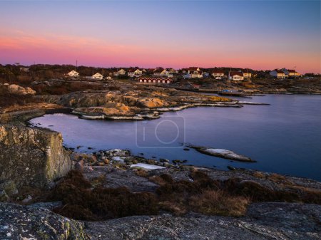 Le ciel du soir est peint en oranges et rouges, reflétant la mer calme. Maisons perchées sur la côte cèdent la place à un paysage suédois magnifique.