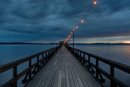 Téléchargez les photos : Longue jetée en bois au-dessus d'un lac la nuit avec des lumières suspendues au-dessus. Suède. - en image libre de droit