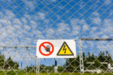 Warning sign on fence in front of high voltage transformer substation