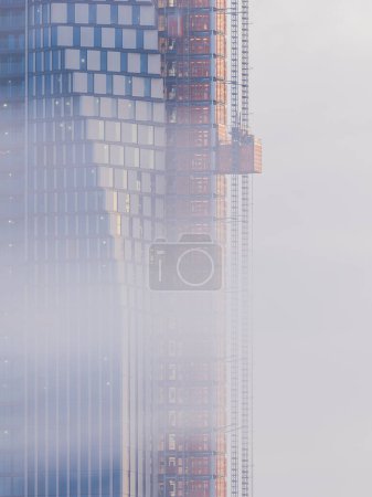Photo for An unfinished skyscraper in Gothenburg, Sweden is reflected off the foggy sky amidst a backdrop of billowing clouds and engineering work-in-progress. - Royalty Free Image