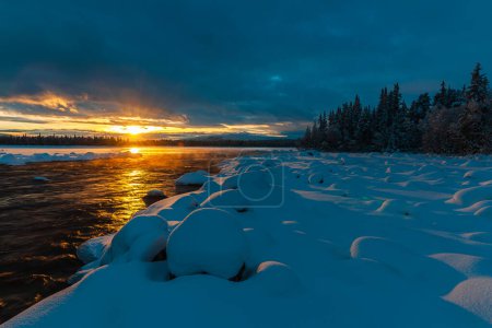 Photo for A captivating winter scene in Norway of a snow-covered landscape reflected in the icy river, adorned with vibrant blue sky and clouds at sunset. - Royalty Free Image