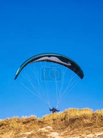 Foto de Un emocionante parapente se eleva en lo alto del cielo sobre Skagen, Dinamarca, con alegría y libertad. El ambiente azul crea un ambiente para deportes extremos y actividades de ocio. - Imagen libre de derechos