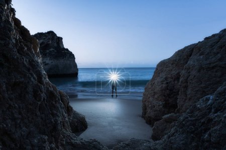 Foto de Hombre con faro iluminado, parado en la playa junto al borde de las aguas al atardecer, Alvor, Algarve, Portugal, Europa - Imagen libre de derechos