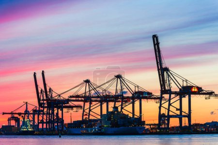 Photo for A commercial harbor at sunset: cargo containers, cranes, and a nautical vessel. - Royalty Free Image